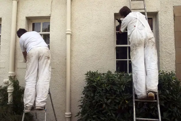Two decorators on ladders painting the outside of a rendered house