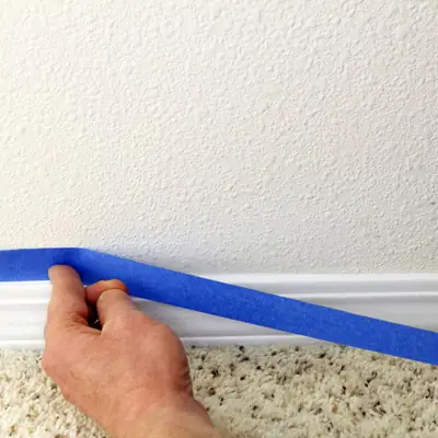 Masking tape being applied along a skirting board before painting
