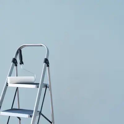 Step ladder and paint roller against a freshly painted blue wall