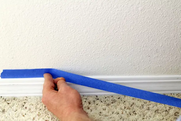 Masking tape being applied along a skirting board before painting